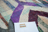 Dense, hand-woven rag rug texture with violet, cherry red, ivory, and green chevron detail.
