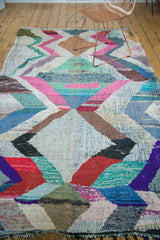 Hand woven Moroccan rag rug with geometric zigzag pattern, red, purple, and black fringe.