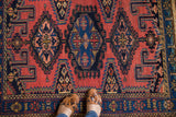 Vintage Persian rug featuring an indigo geometric border and intricate brick red field pattern.