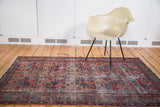 Corner of distressed antique Persian Lilihan rug with worn floral motifs, jewel tones.