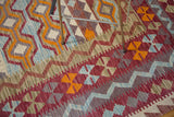 Kilim carpet detail: dynamic tribal zig-zag pattern in burgundy, blue, orange, and beige.