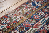 Geometric bands of brilliant red, blue, and mustard on a distressed antique Shirvan rug.