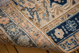 Curled edge reveals vintage Heriz rug's hand-knotted pile with navy blue and sand patterns.