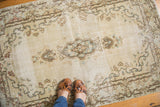 Distressed Kerman rug with an ivory field, diminutive medallion, and rococo motifs.