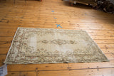 Distressed ivory Kerman rug corner displaying rococo scrollwork and subtle muted tones.