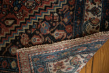 Folded vintage Malayer rug corner reveals hand-knotted back, secure fringe, and blue border.