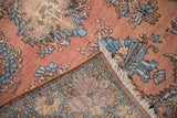 Vintage Kerman rug corner showcasing coral floral pile, white fringe, and tightly woven foundation.