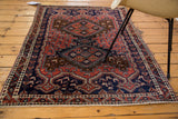 Vintage Afshar rug corner showing brick red geometric patterns, navy dragon border, and ivory fringe.