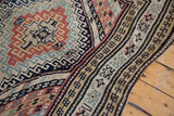 Caucasian carpet's geometric borders and chevron patterns in navy, tangerine, and ivory tones.