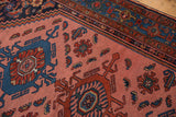 Blush rose field featuring intricate geometric motifs in cobalt and brick red, patterned border.