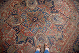 Distressed Heriz carpet showing its geometric quatrefoil medallion in brick red and blue.