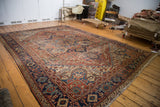 Distressed Persian Heriz rug corner, with geometric floral motifs, fringe, and faded brick red and navy blue.