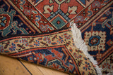 Distressed Heriz carpet corner with hand-knotted pile, ivory fringe, and geometric border.