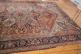 Distressed vintage Heriz rug corner, geometric navy border, brick red field, sky blue accents.
