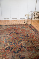 Distressed Heriz carpet's geometric design in softened brick red, navy blue, and ivory tones.