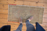 Textured vintage Oushak mat with geometric celadon green pattern and unique red weft edge.