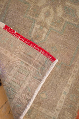 Oushak rug mat's corner folded back, revealing red and orange woven weft edge.