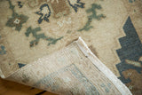 Vintage hand knotted Oushak rug corner reveals fringe, foundation, and ivory, blue, brown floral design.