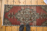 Oushak rug mat with abrashed dusty rose field and central medallion, with dark shoes.