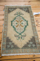 Oushak rug mat corner with beige field, emerald green rams horn, and pinwheel motifs.