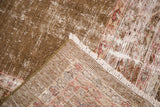 Distressed brown and ivory pile revealing foundation with secured green edge and white fringe.