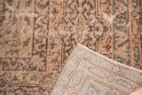 Ornate brown and beige distressed Oushak carpet showing exposed foundation and woven back.