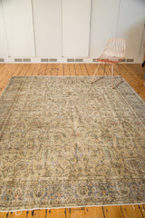 Distressed vintage Oushak carpet with intricate scrolling flowers and muted beige, green, and blue tones.