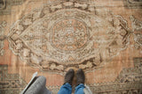 Scalloped oblong medallion with meandering vinery on distressed Oushak rug in apricot and brown.