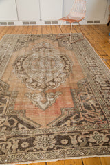 Distressed vintage Oushak rug corner with fringed end, brown border, peach and green tones.