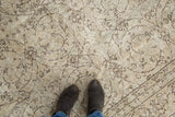 Distressed Oushak rug's faded floral pattern in ivory, beige, and brown, with feet.