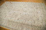 Distressed vintage Oushak carpet corner with faded scrolling vines and floral motifs in beige and brown.