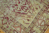 Distressed Oushak rug corner showing raspberry red, celadon green, and antique ivory motifs.