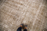 Feet on distressed Khorassan carpet, showing faded allover pattern, soft cream and charcoal tones.
