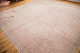 Distressed vintage Oushak rug corner displaying faded cream, pink, and lavender patterns.