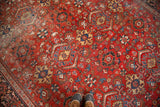 Distressed vintage Mahal carpet, bold cherry red field, worn patterns, feet visible.