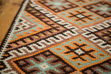Hand-knotted Kilim rug close-up showing tangerine, charcoal, ivory check and latch designs.