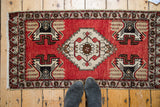 Hand-knotted Oushak rug showcasing cherry red field, geometric medallion, with shoes for scale.