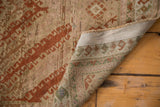 Finely woven distressed Afghani rug corner, showing secured edge and geometric patterns in sage, terracotta, beige.