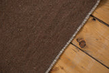 Secured edge of hand woven chocolate brown Moroccan Kilim, with natural wool inflections.