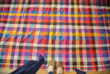 Hand woven Moroccan plaid textile with vibrant squares and tattered lower left edge.