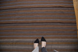 Hand-woven Moroccan Kilim featuring striated brown and natural stripes, with a person's feet.