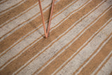Textured vintage flatweave carpet showing varying ivory and caramel stripes with black wool flecks.