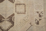 Simplistic charcoal brown geometric forms visible on a faded ivory hand-knotted rug surface.