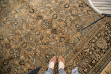 Vintage Meshed rug's bronze and charcoal herati pattern, with feet in brown shoes.
