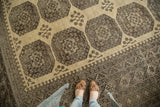 Distressed Afghan carpet with intricate rectilinear borders, octagonal guls, and muted abrashes.