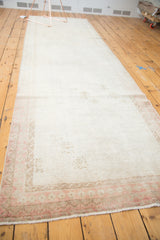 Distressed Oushak runner, faded ivory field with blush geometric border and short pile.