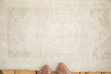 Vintage Oushak rug's even short pile, showing pale sand, ivory, and faint green motifs.