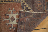 Hand-knotted vintage Oushak rug folded, revealing copper and ivory geometric motif with dark, woven reverse.