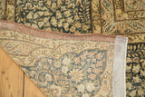 Distressed Kerman carpet corner showing ornate floral pattern, secured edge, and hand-knotted foundation.