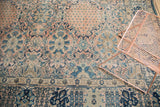 Blush and ink blue scrolling vinery on a vintage Kashan carpet's ornate field.